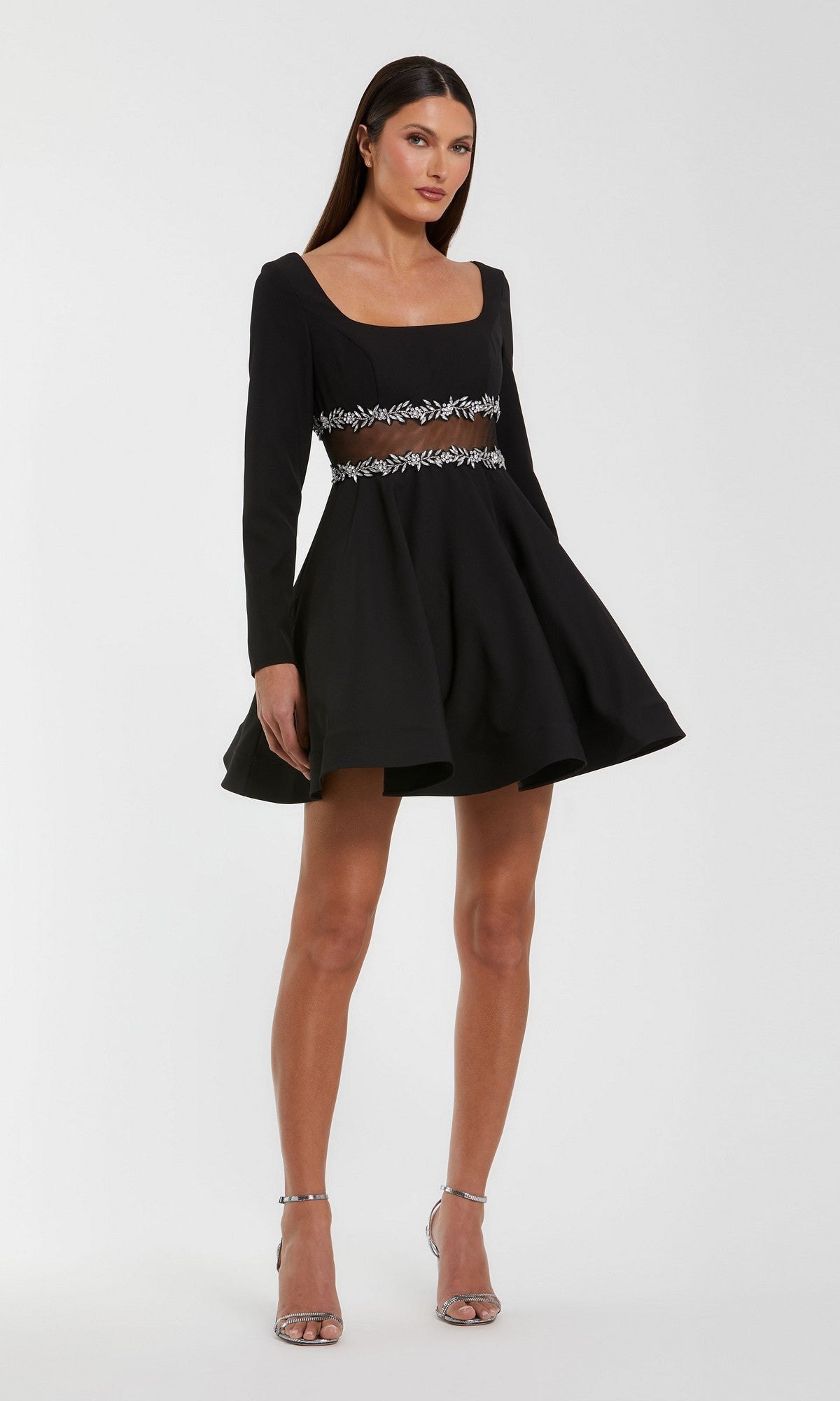 Woman wearing the Short Party Dress: Mac Duggal 50047 in black, featuring a fit-and-flare silhouette with a square neckline, beaded sheer waistline, and flared skirt, paired with silver high-heeled sandals and standing against a plain background.